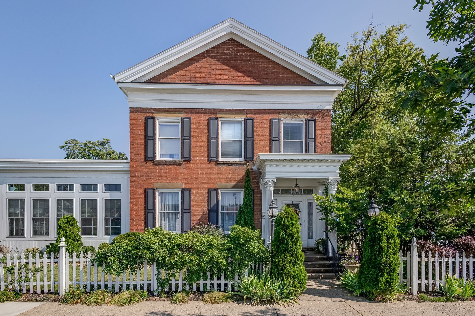 Red brick two-story house with white trim, shutters, and a picket fence in front.