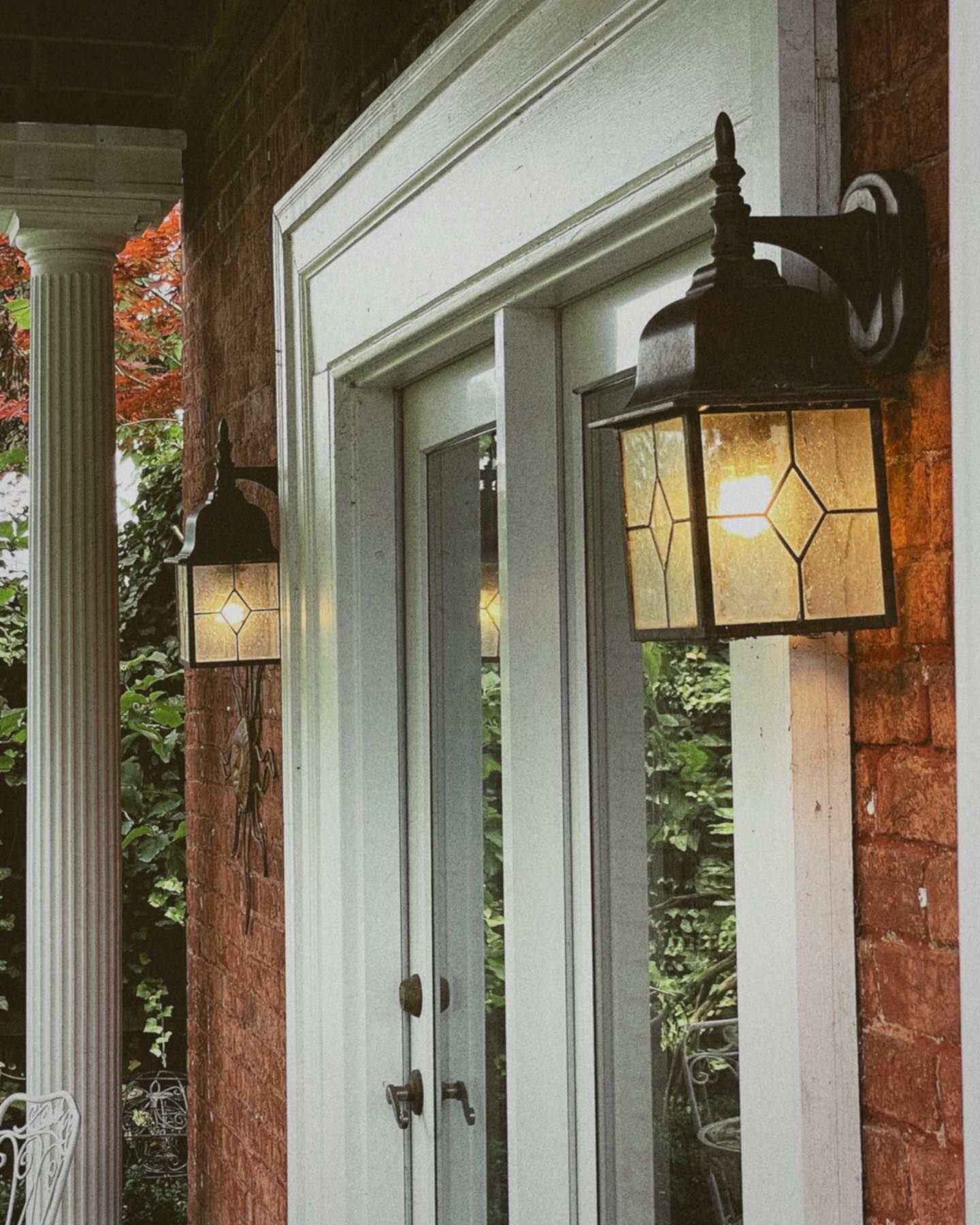 Two outdoor wall lanterns illuminate a white-framed doorway set in a brick wall.