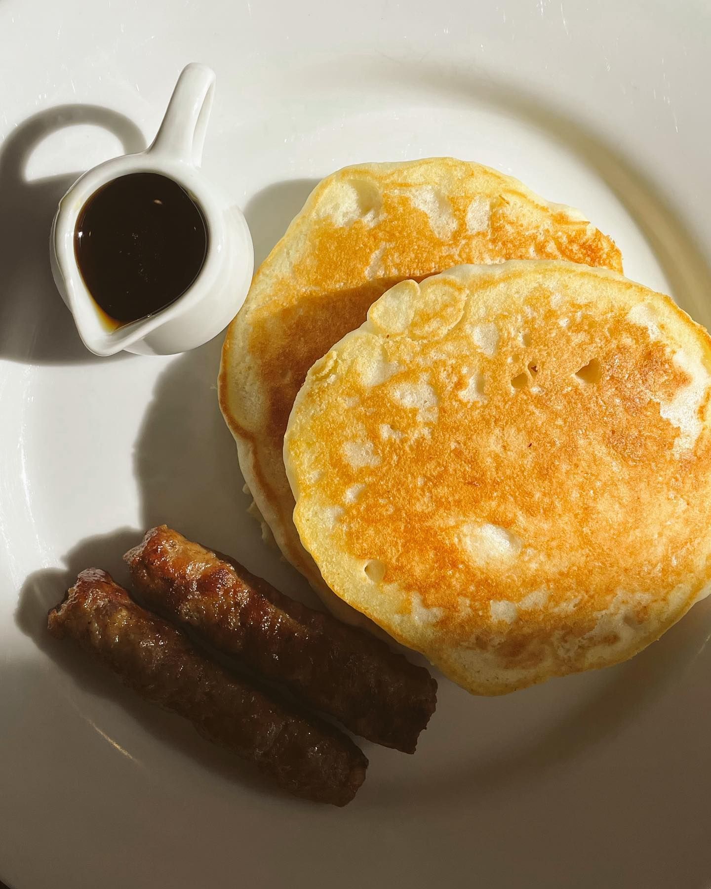 Pancakes, sausage, and syrup on a white plate; breakfast.