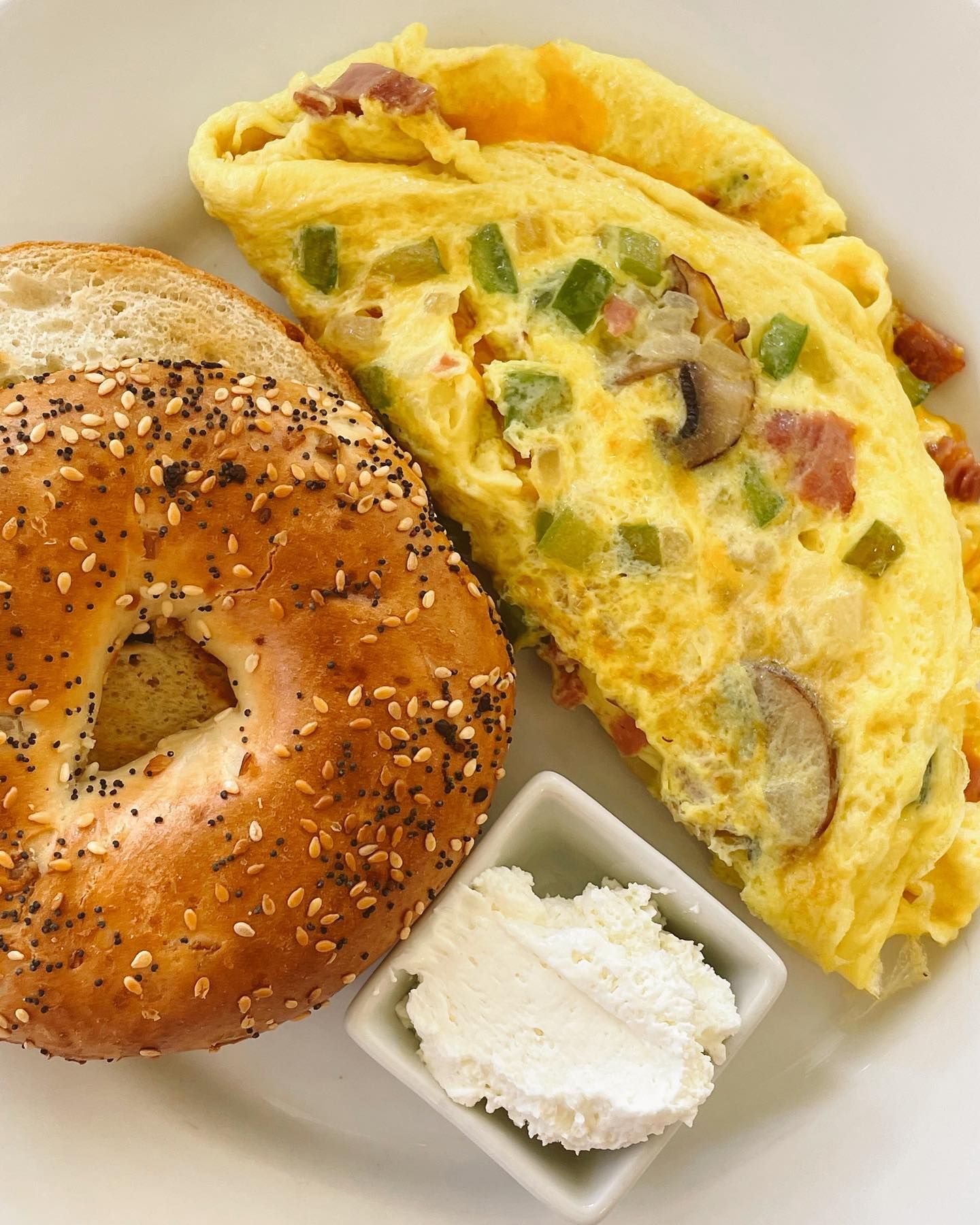 Omelet with green peppers, mushrooms, and bacon, bagel with seeds, and cream cheese.