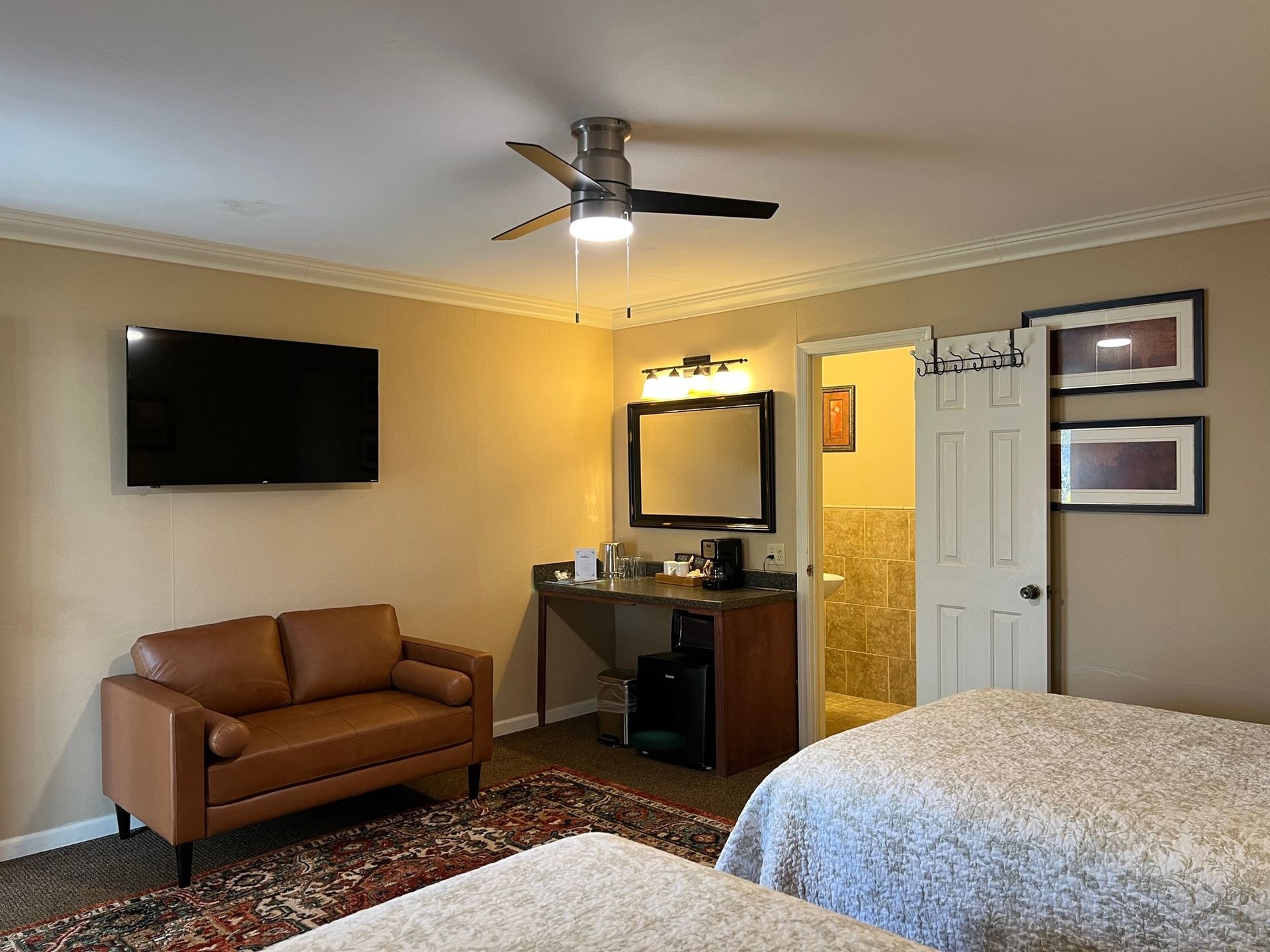 Hotel room with two beds, small sofa, TV, desk area with mirror, and a bathroom.