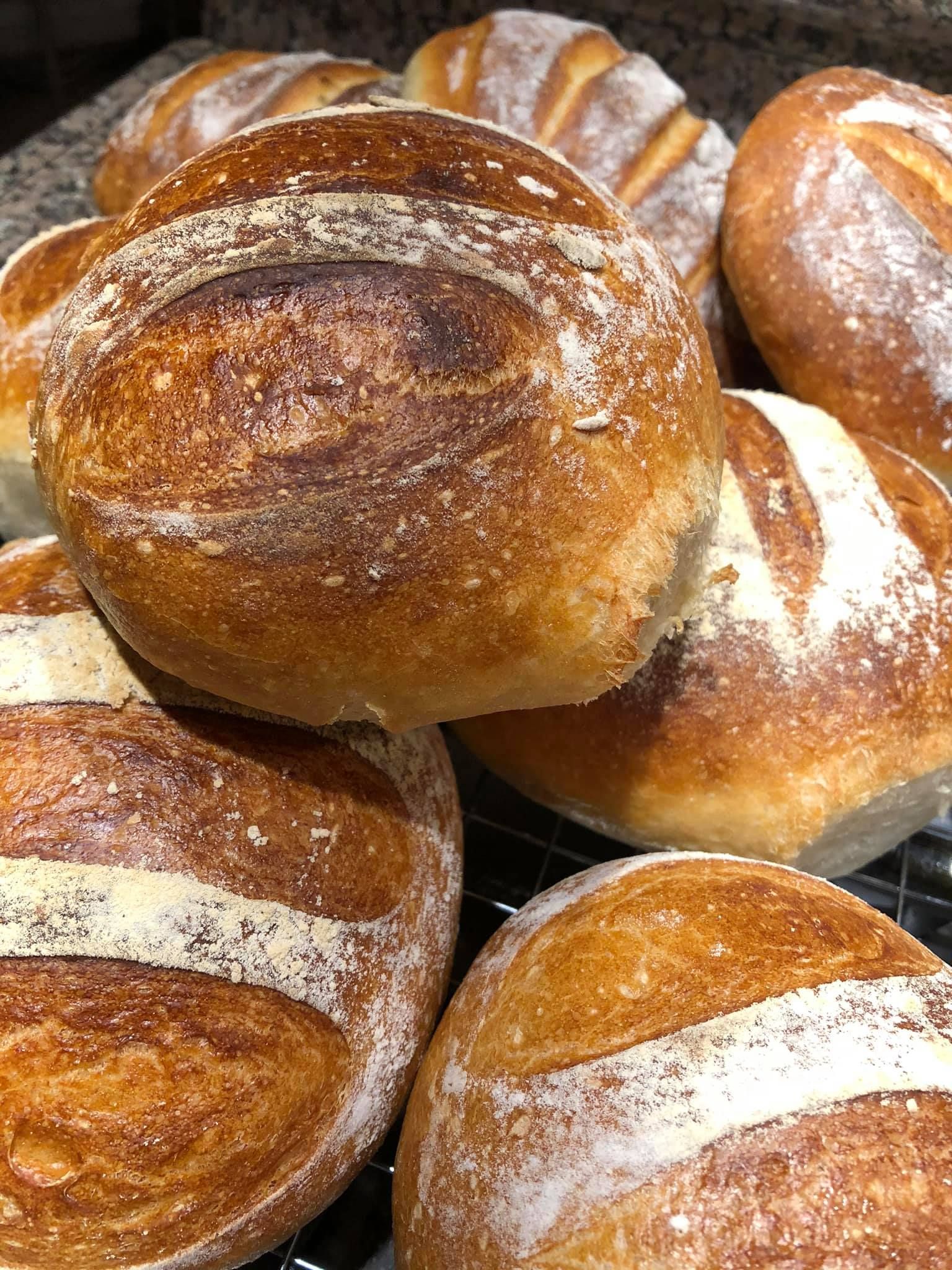 Pile of freshly baked, golden brown loaves of artisan bread with scored tops.