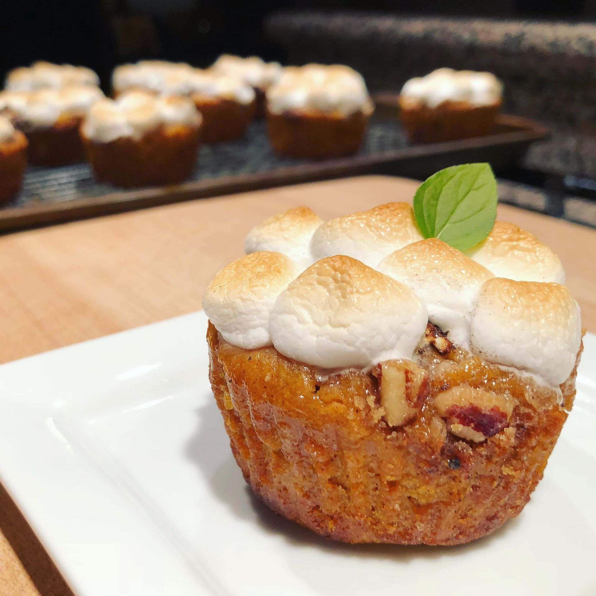 Mini sweet potato muffin with toasted marshmallows, pecans, and mint leaf. Other muffins in background.