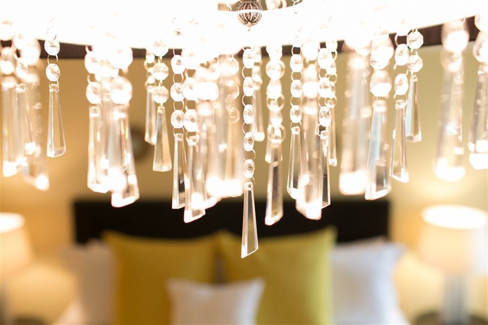 Crystal chandelier hanging above bed with yellow and white pillows.