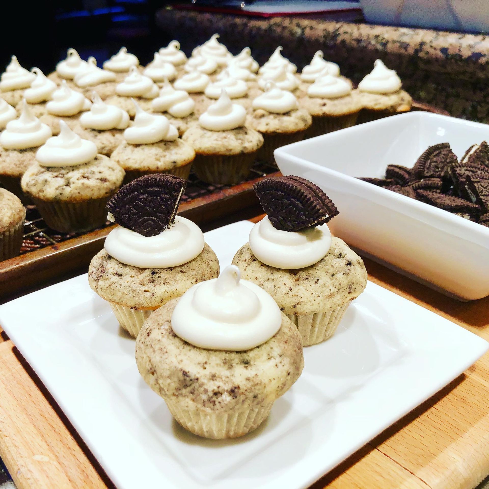 Cupcakes with white frosting and Oreo cookies on a white plate and in a bowl.