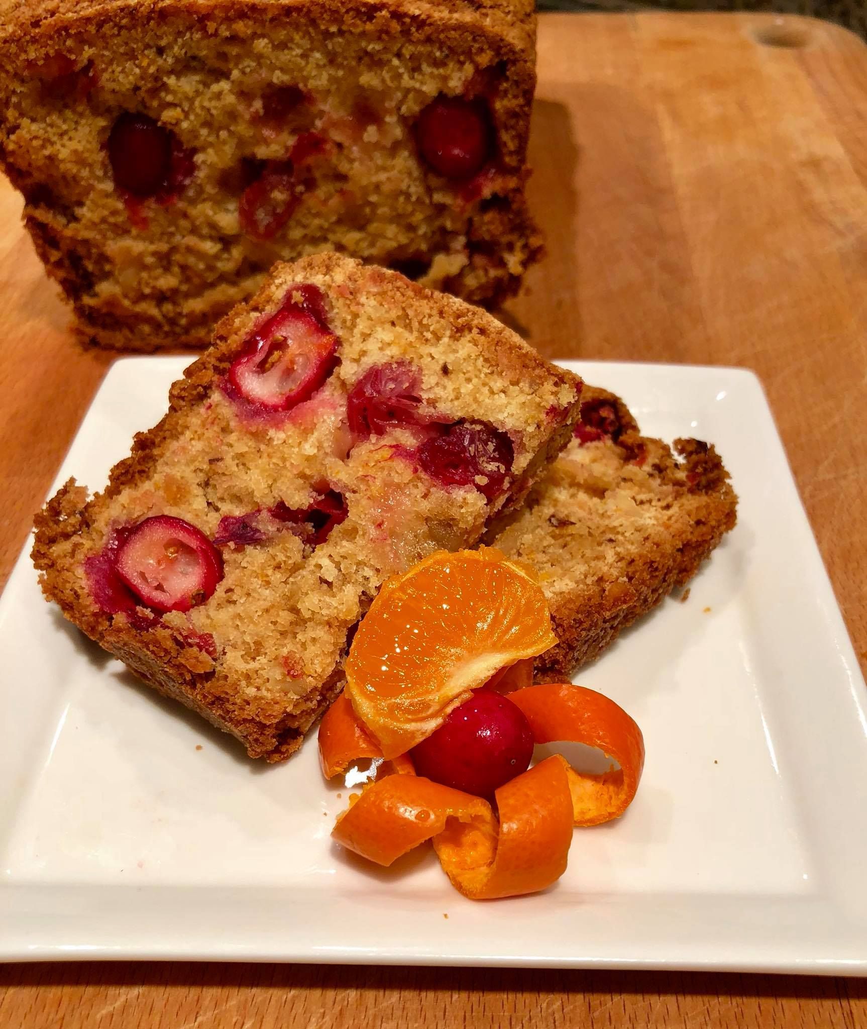 Cranberry bread slices on a white plate with orange slices and cherry garnish. Wooden background.