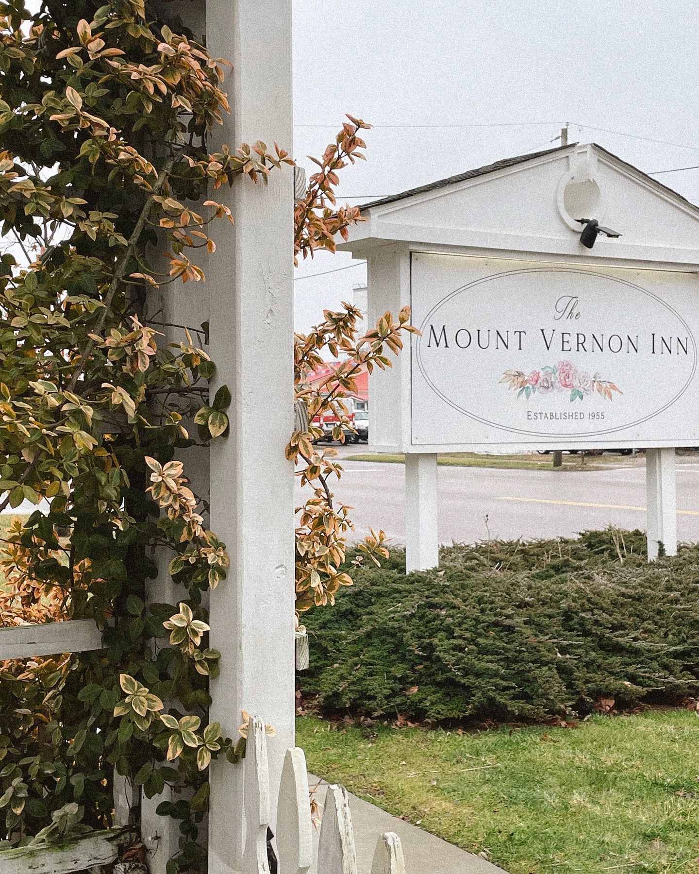 Sign for Mount Vernon Inn, with ivy-covered white picket fence post and trimmed bushes.
