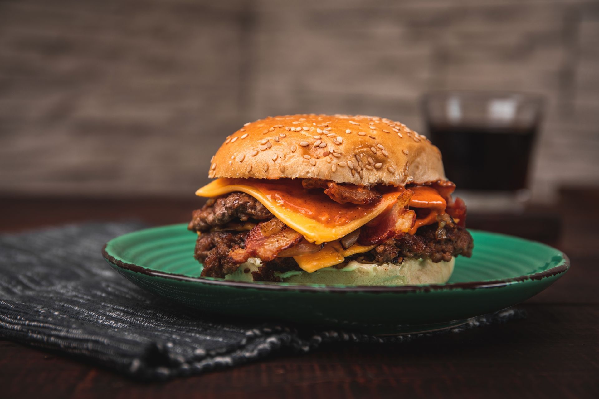 Double cheeseburger with bacon on a green plate, with a drink in the background.