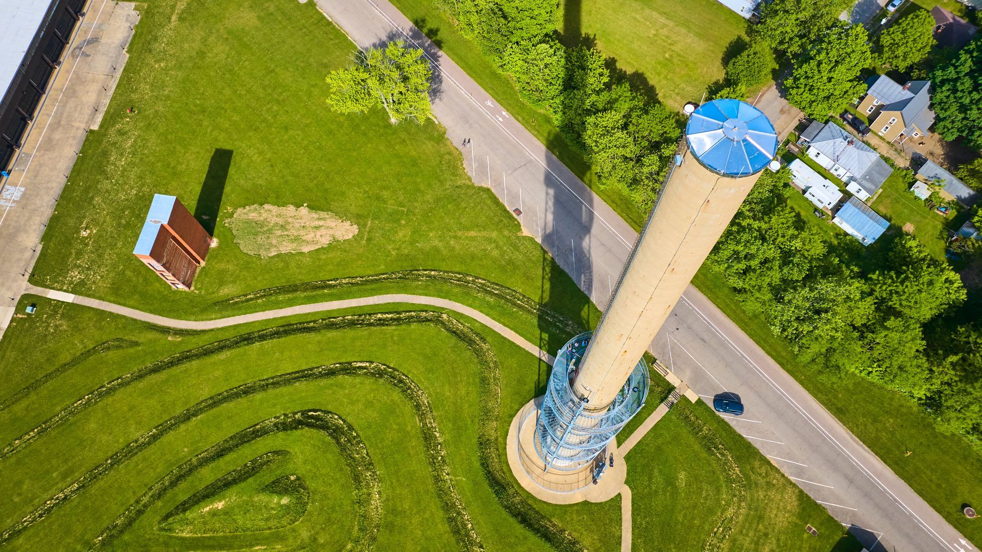Aerial view of a tall smokestack beside a road and green fields.