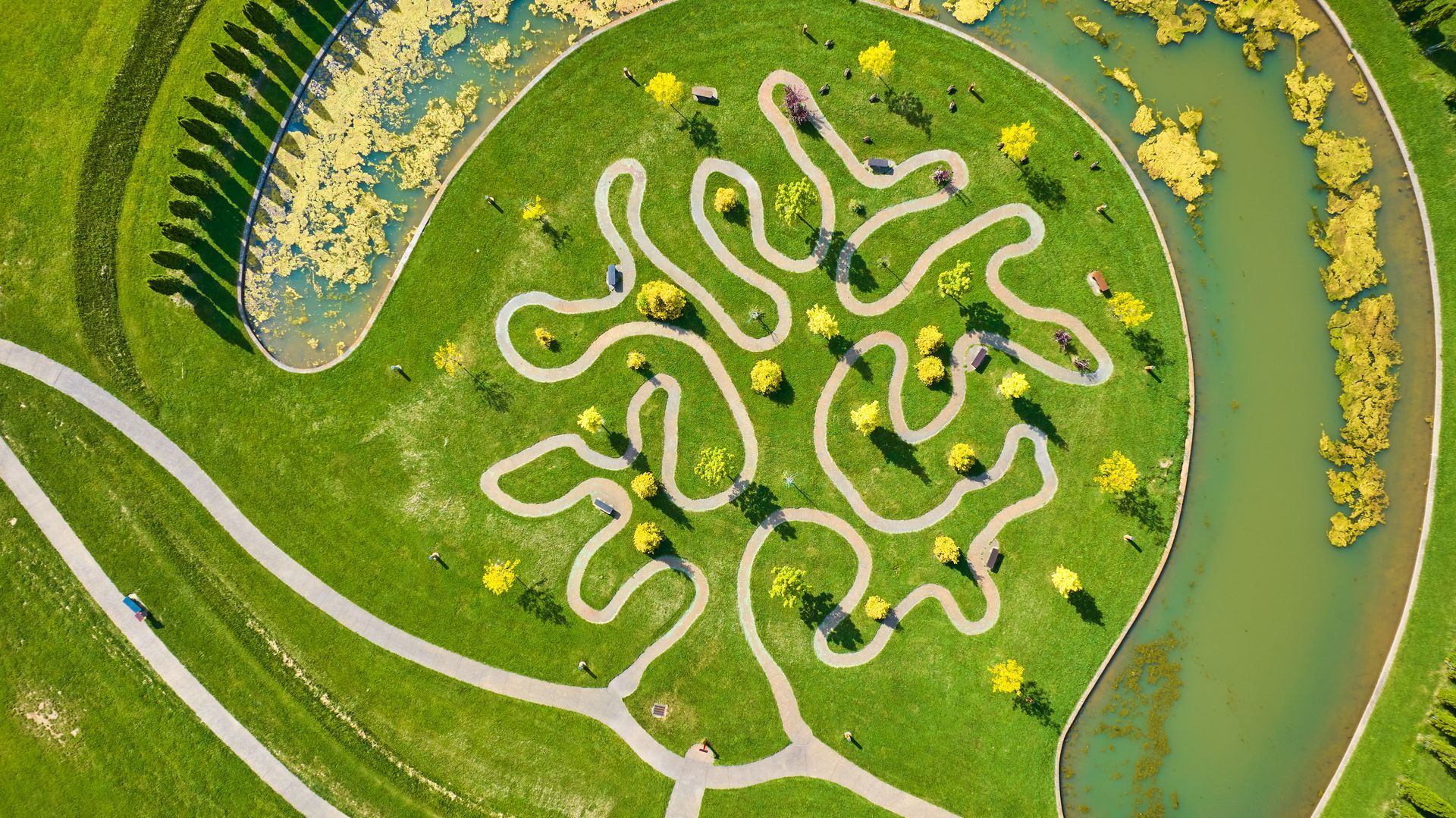 Aerial view of a winding white path through a green park beside a curving river