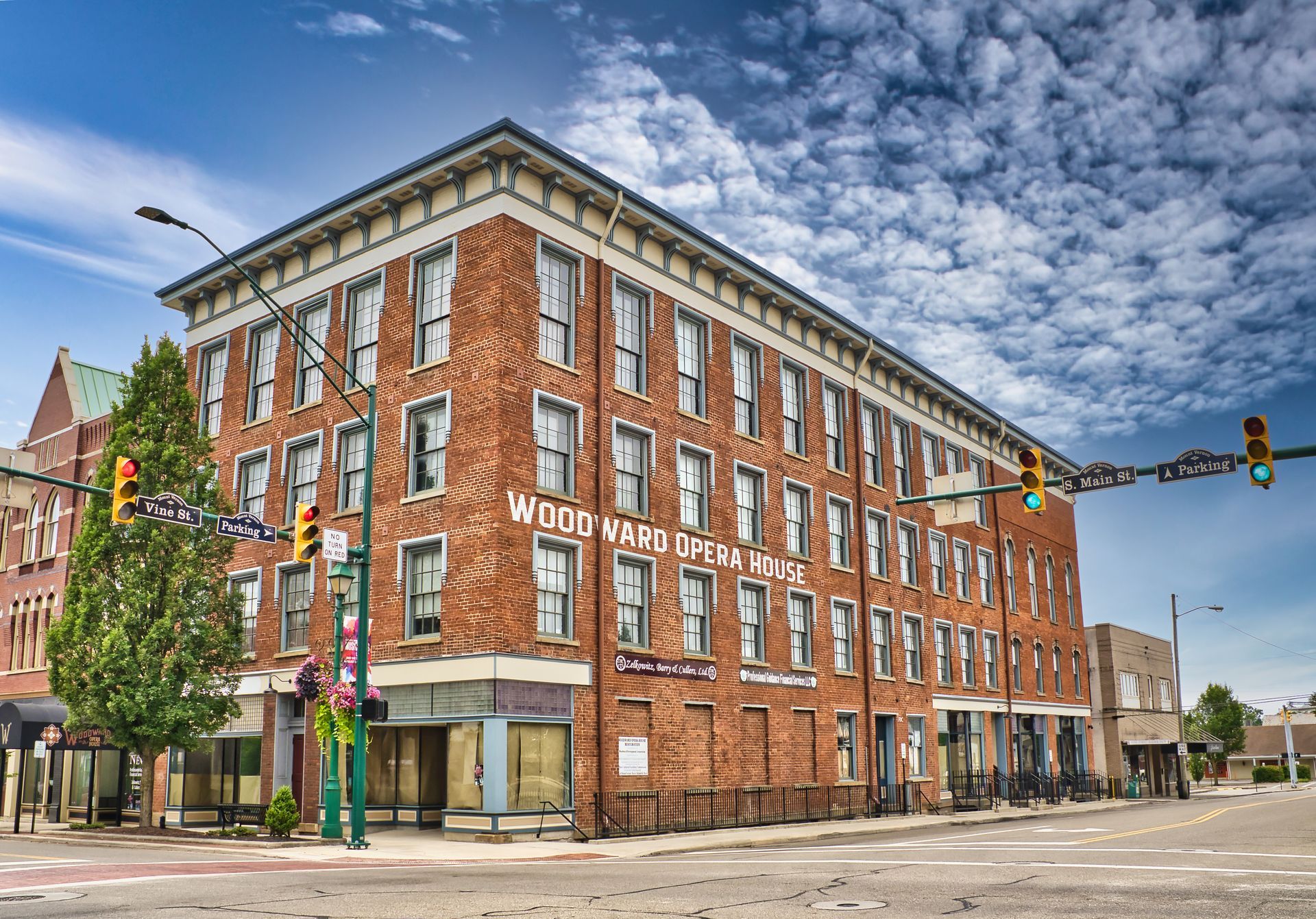 Red brick corner hotel with white trim on a city street under a partly cloudy sky
