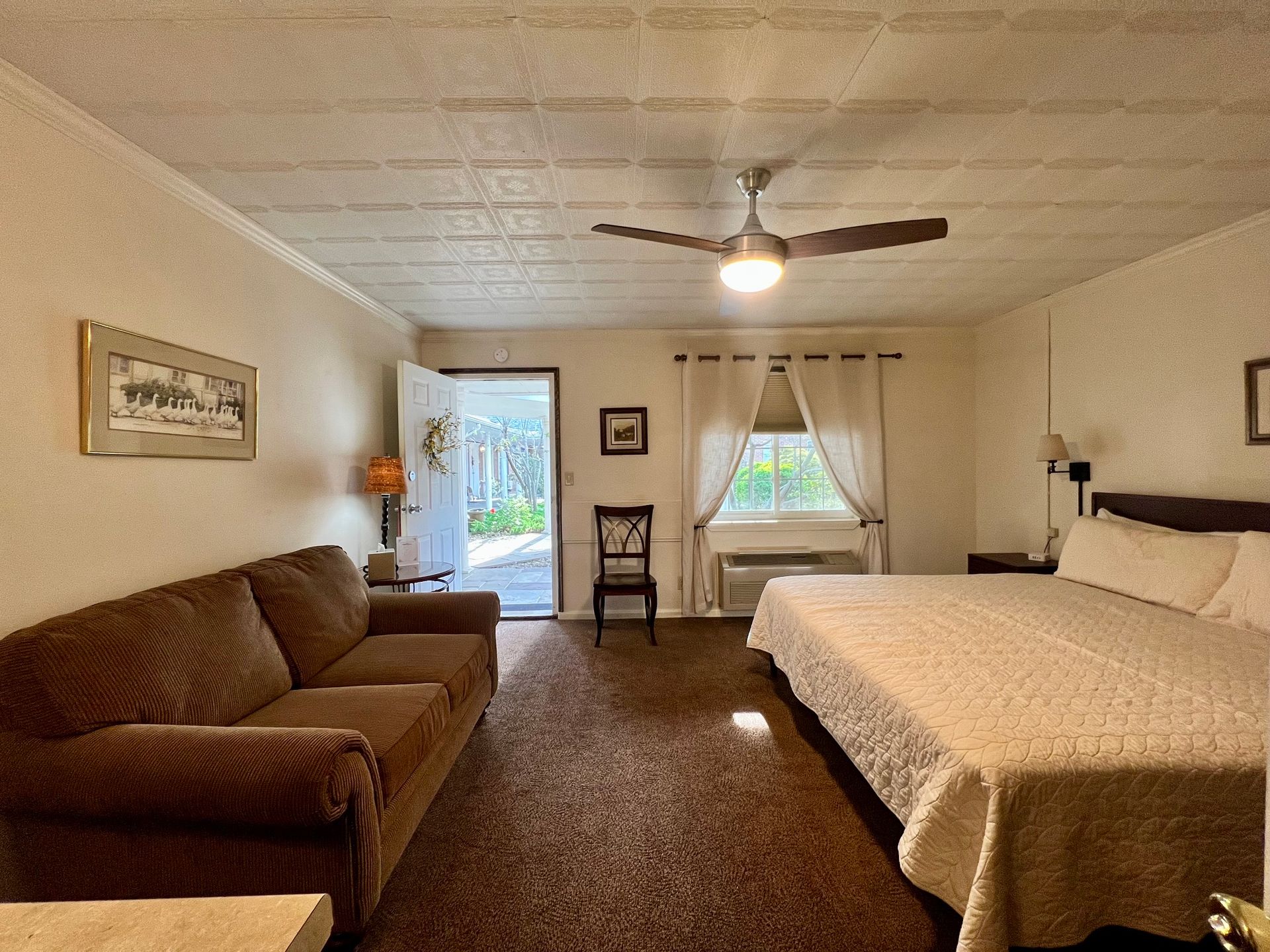 Bedroom with a bed, desk, window with curtains, ceiling fan, and lamp.