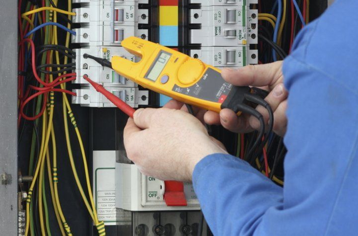 Electricista utilizando un multímetro para probar el cableado dentro de un panel eléctrico.
