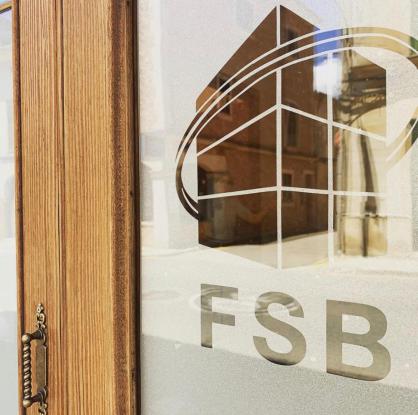 Puerta con logotipo grabado y reflejo del edificio; marca FSB.