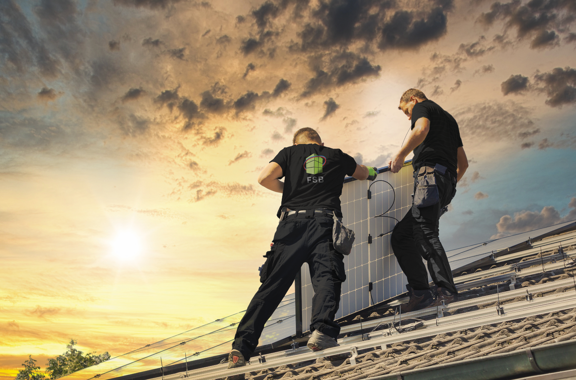 Zwei Arbeiter installieren Solarpaneele auf einem Dach vor einem bewölkten Sonnenuntergang.