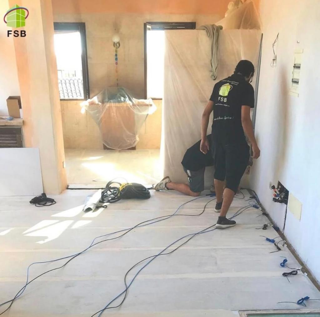 Dos trabajadores instalando cableado eléctrico en una habitación, herramientas y muebles cubiertos presentes.