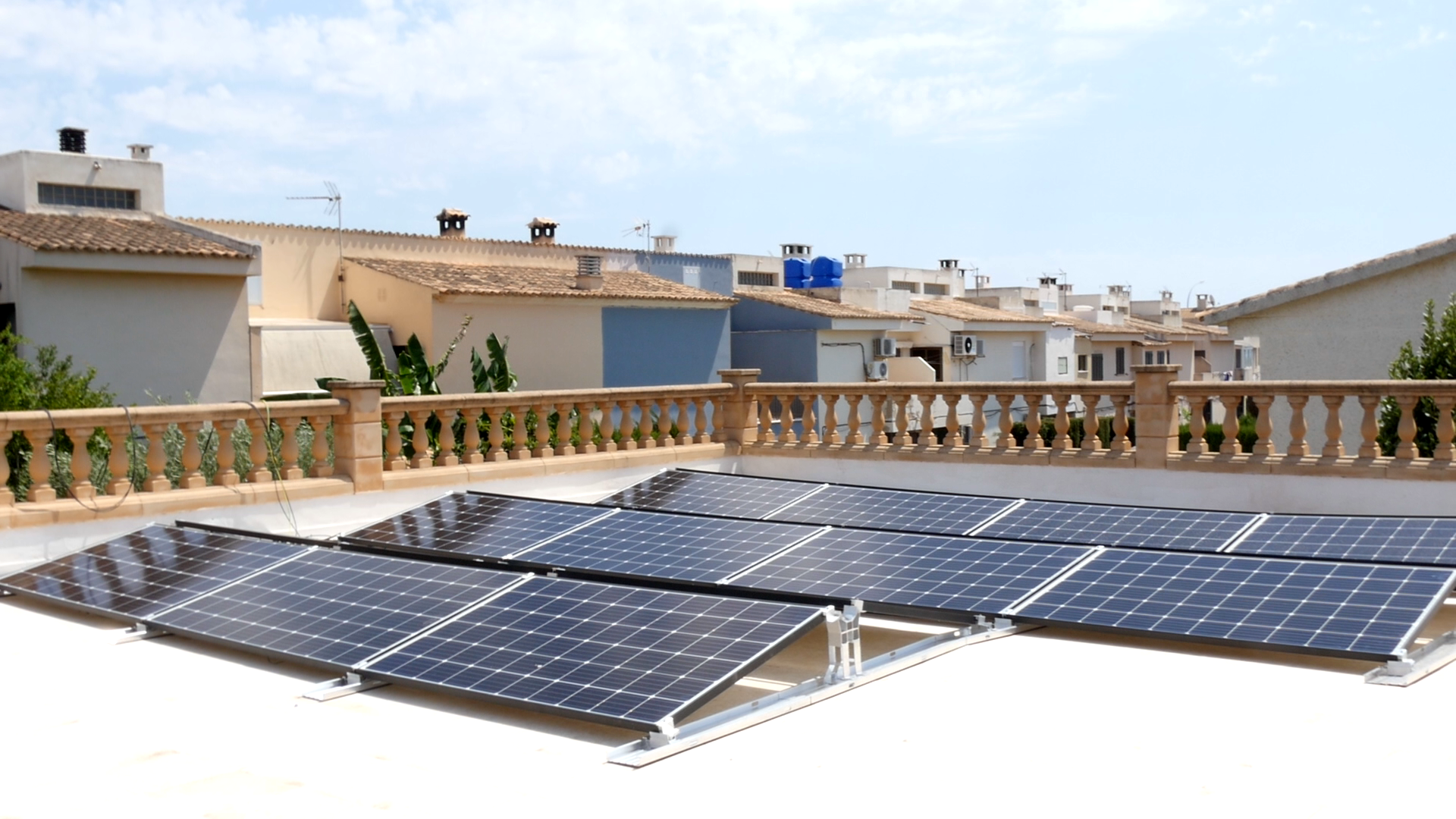 Paneles solares instalados en un tejado blanco, en un día soleado. Otros edificios al fondo.