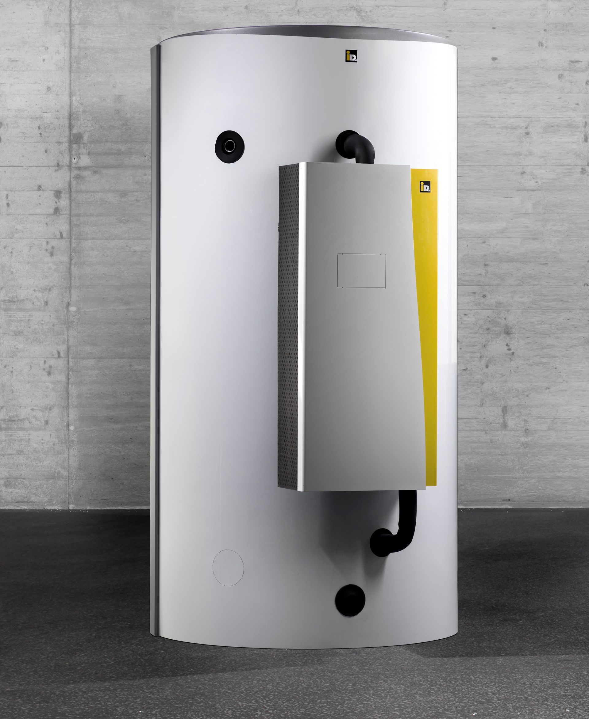 Ein zylindrischer Warmwasserbereiter mit Bedienfeld, vor einer Betonwand und dunklem Boden.