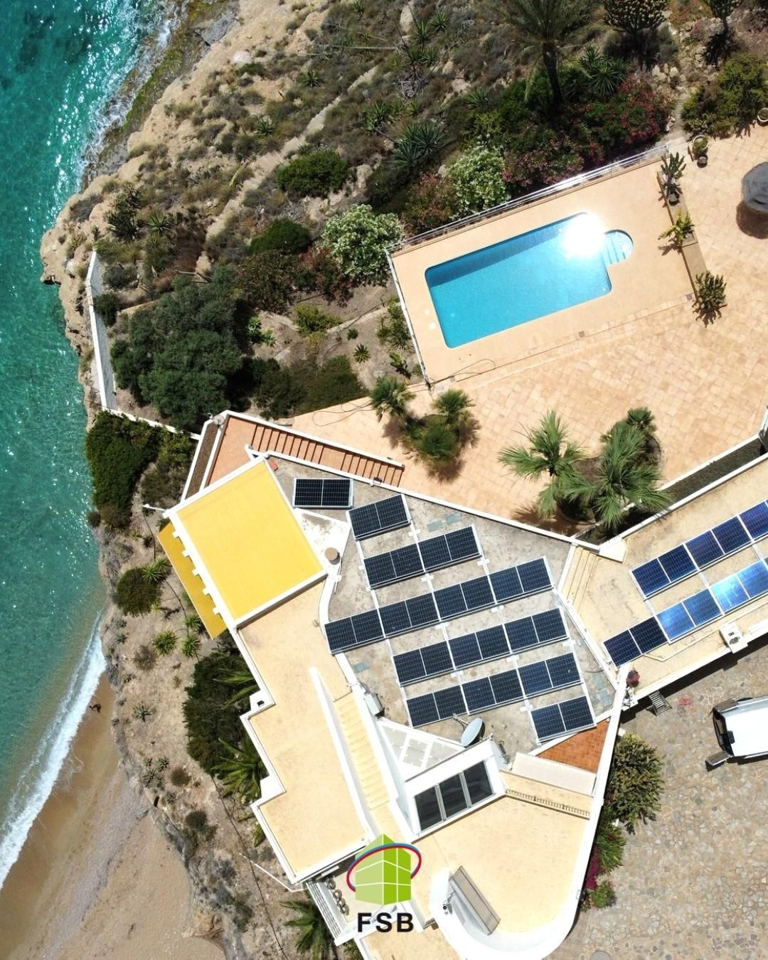 Vista aérea de una villa costera con paneles solares en el techo, piscina y vistas al mar.
