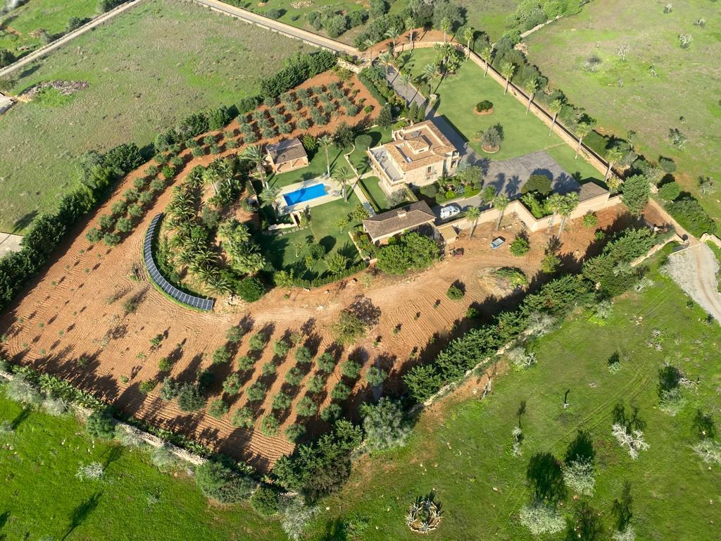 Vista aérea de una villa con piscina, rodeada de jardines y campos, cerrada por muros de piedra.