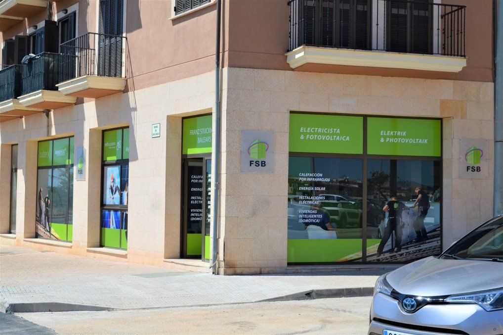 Exterior de una oficina inmobiliaria con grandes ventanales, señalización verde y blanca y un coche aparcado en el frente.