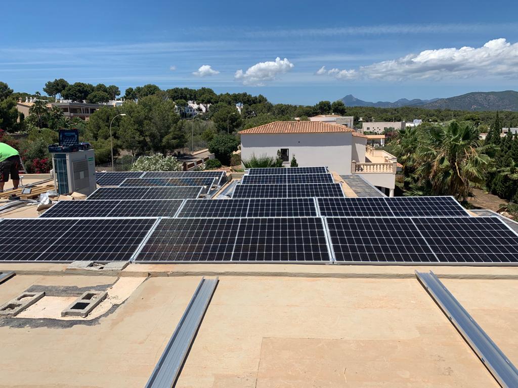 Paneles solares instalados en un techo plano, día soleado, entorno residencial con vistas.