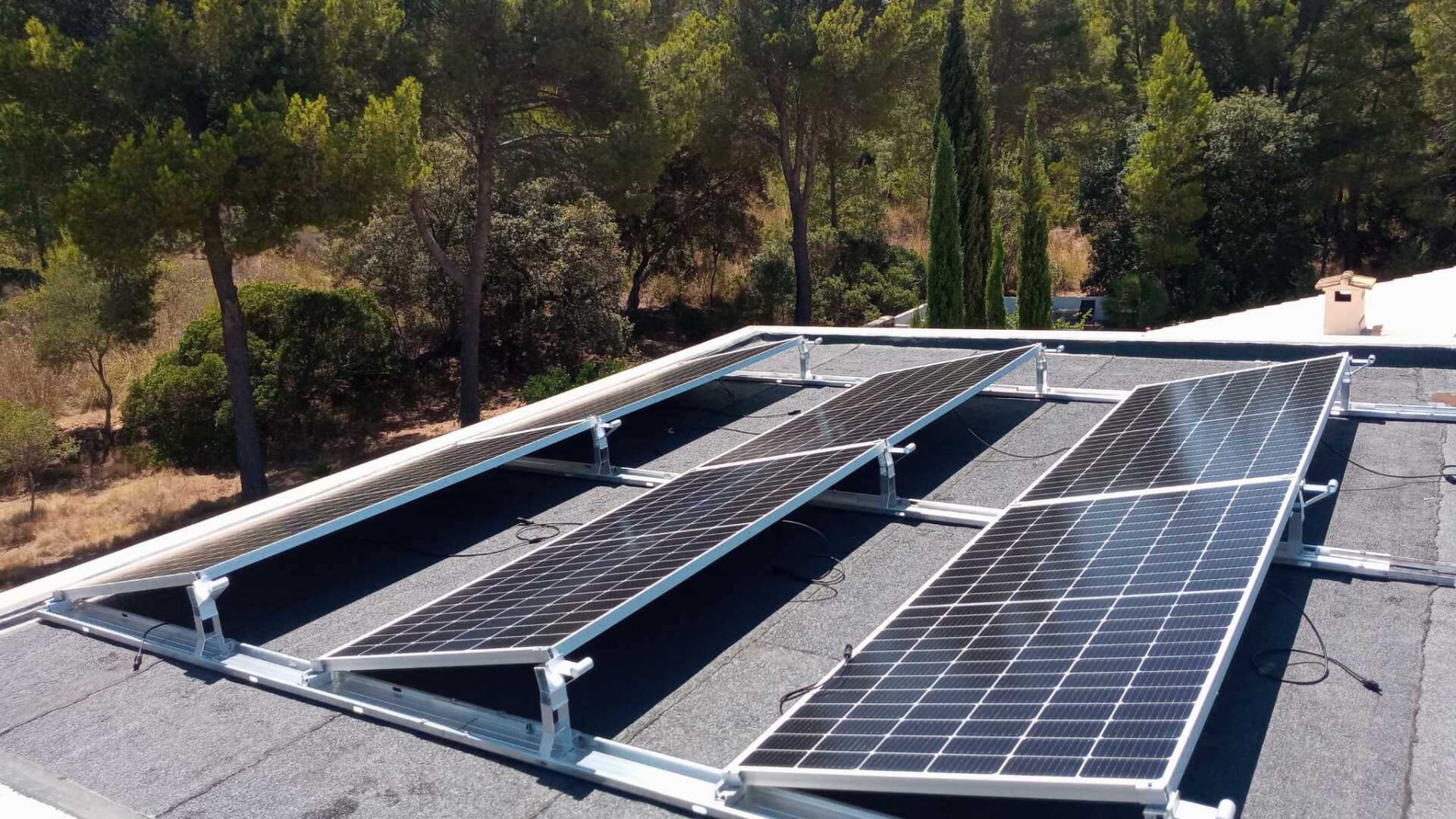 Paneles solares instalados en un tejado con un telón de fondo de árboles y un cielo azul.