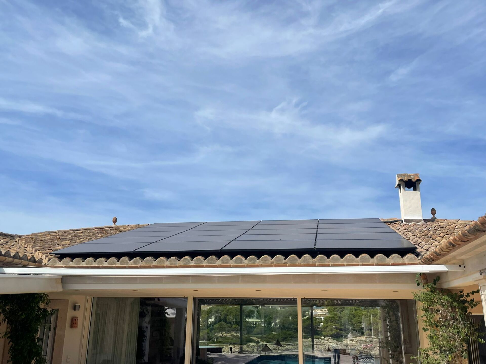 Paneles solares sobre un tejado de tejas bajo un cielo parcialmente nublado.