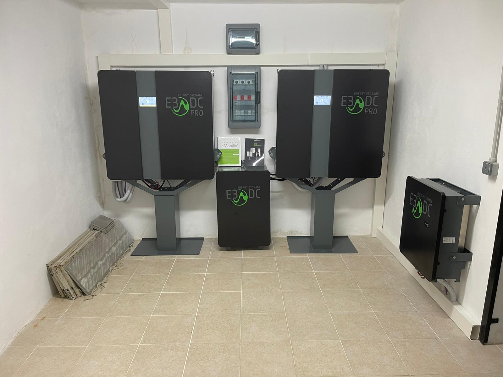 Una pequeña sala con equipos de baterías solares. Dos unidades negras grandes se encuentran sobre pedestales, una más pequeña debajo y otra en la pared.
