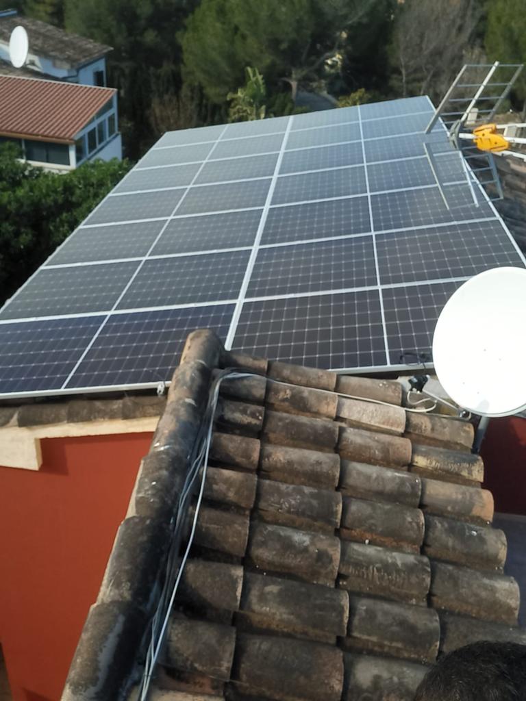 Paneles solares instalados en un tejado de tejas, con vistas a edificios y árboles.