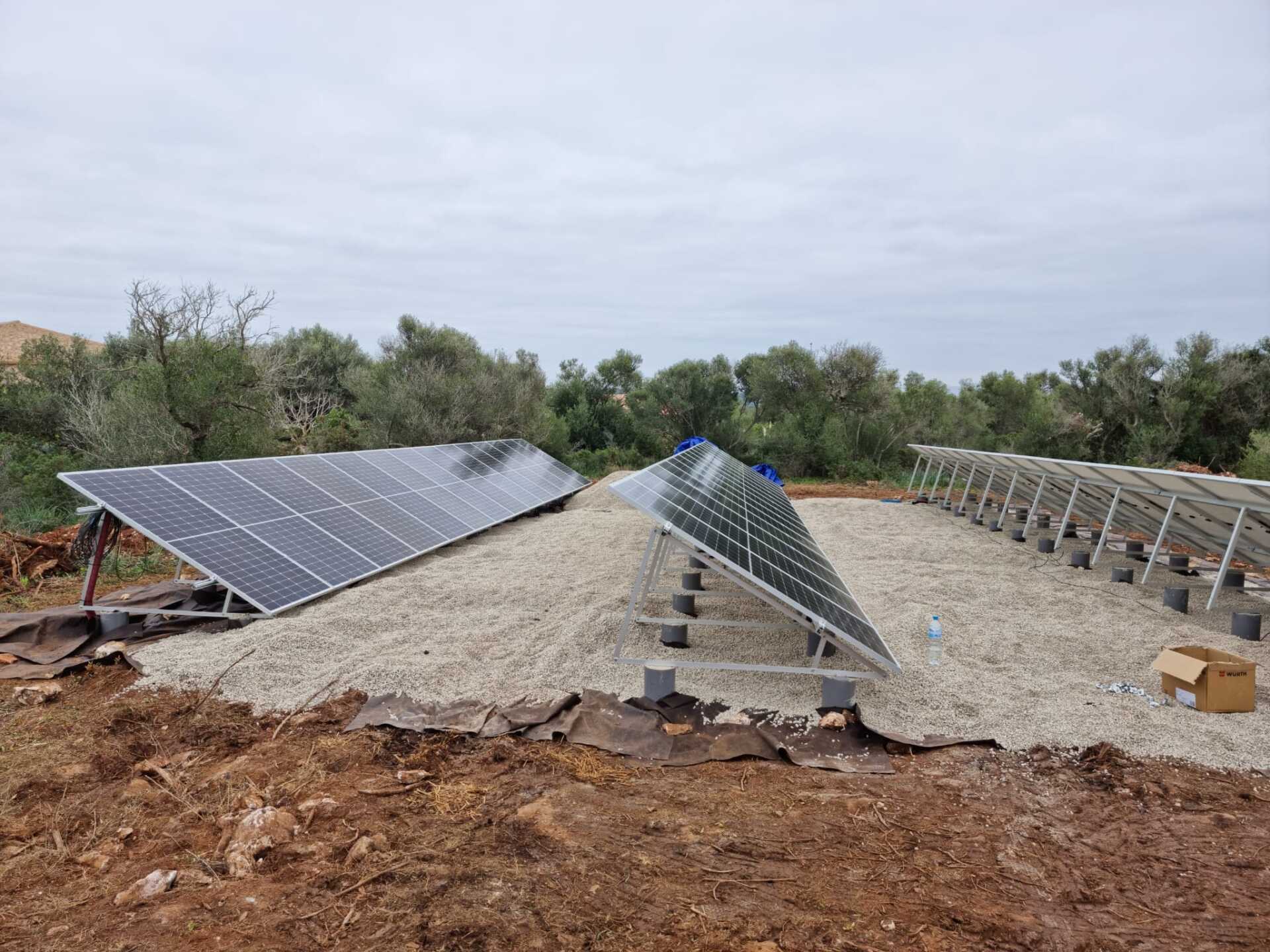 Paneles solares sobre una base de grava en un entorno al aire libre bajo un cielo nublado.