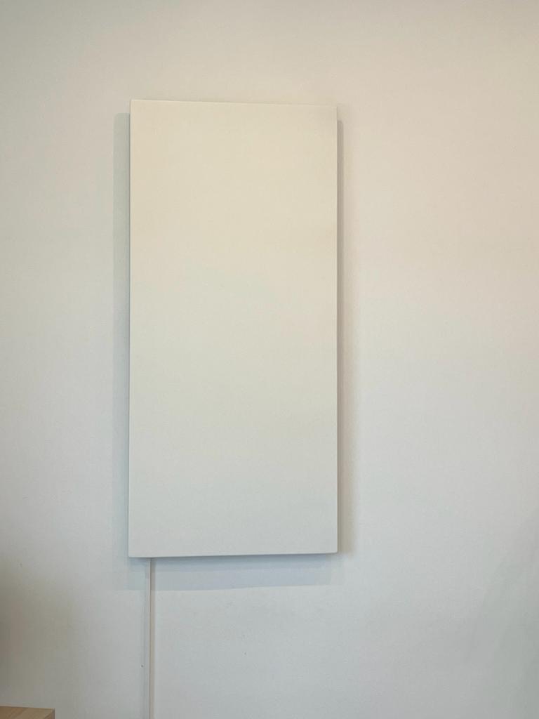 White rectangular panel heater mounted on a white wall; power cord visible.