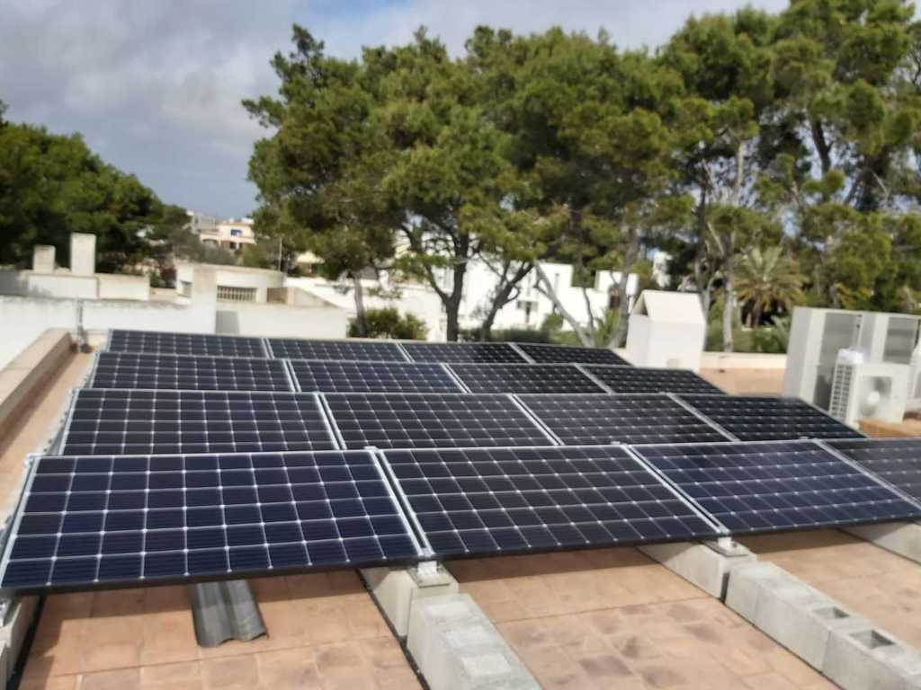Paneles solares instalados en un tejado, con árboles y un edificio visibles al fondo.