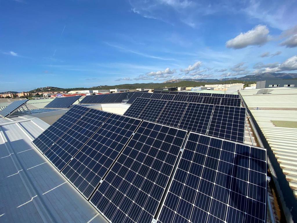 Paneles solares en el tejado de un edificio, cielo azul y nubes de fondo.