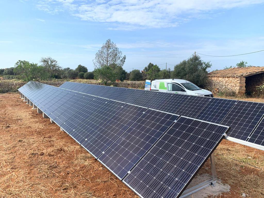 Solar panels installed on brown earth with a van in the background under a blue sky.