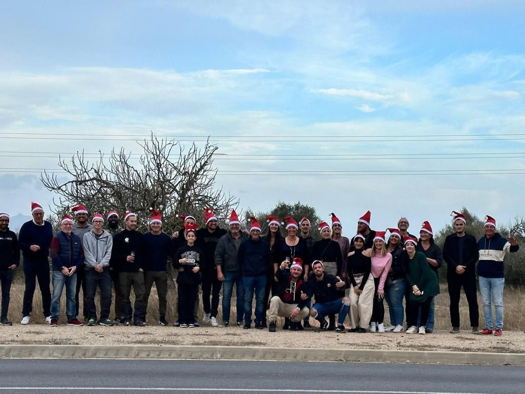 Grupo de personas con gorros de Papá Noel posando al aire libre cerca de una carretera bajo un cielo nublado.