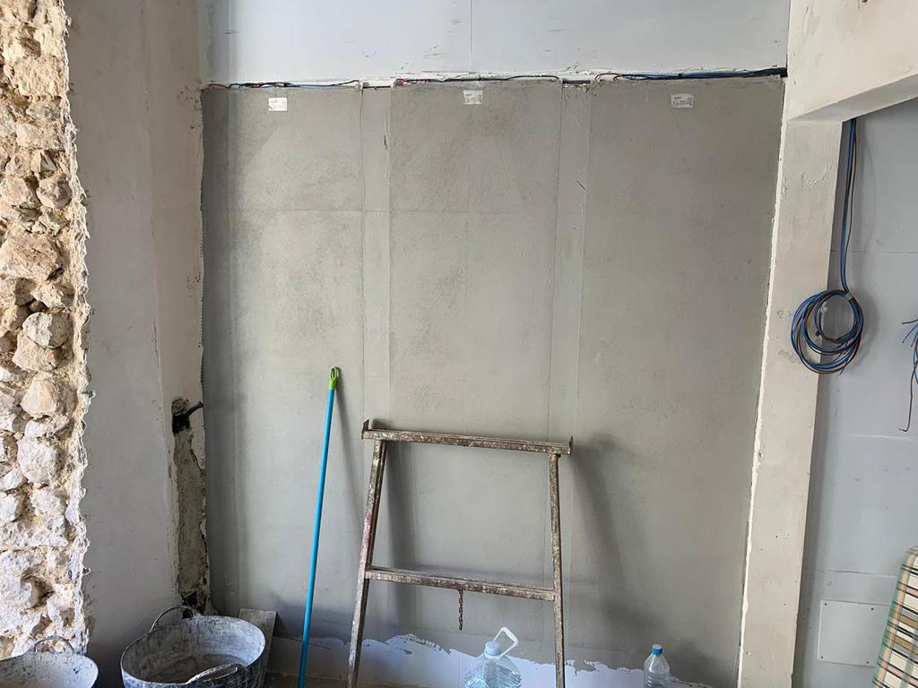 Muro interior en construcción con escalera, yeso y columna de piedra vista.