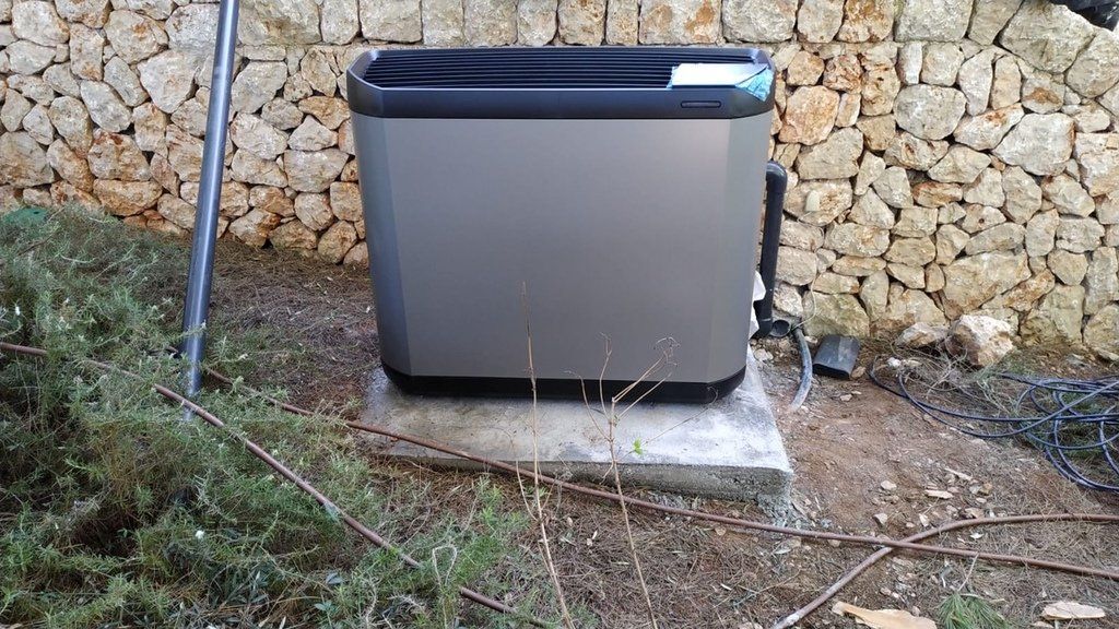 Caja rectangular gris cerca de un muro de piedra, sobre una base de hormigón, al aire libre.