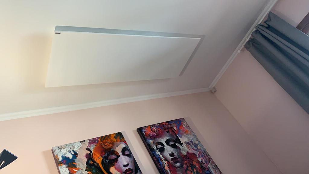 White ceiling-mounted infrared heater in a pink-walled room with art prints.