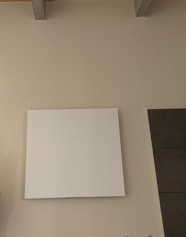 White square panel mounted on a light beige wall, near a dark grey panel.