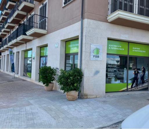 Local comercial en esquina con letrero verde y plantas en macetas. El edificio es beige.