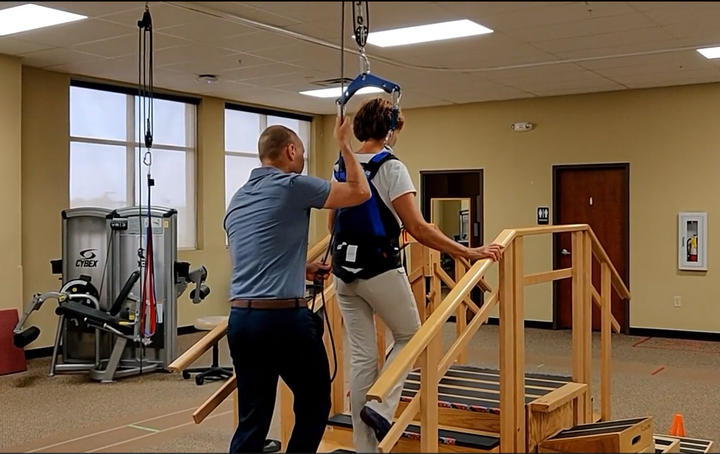 A man is helping a woman climb stairs in a gym.