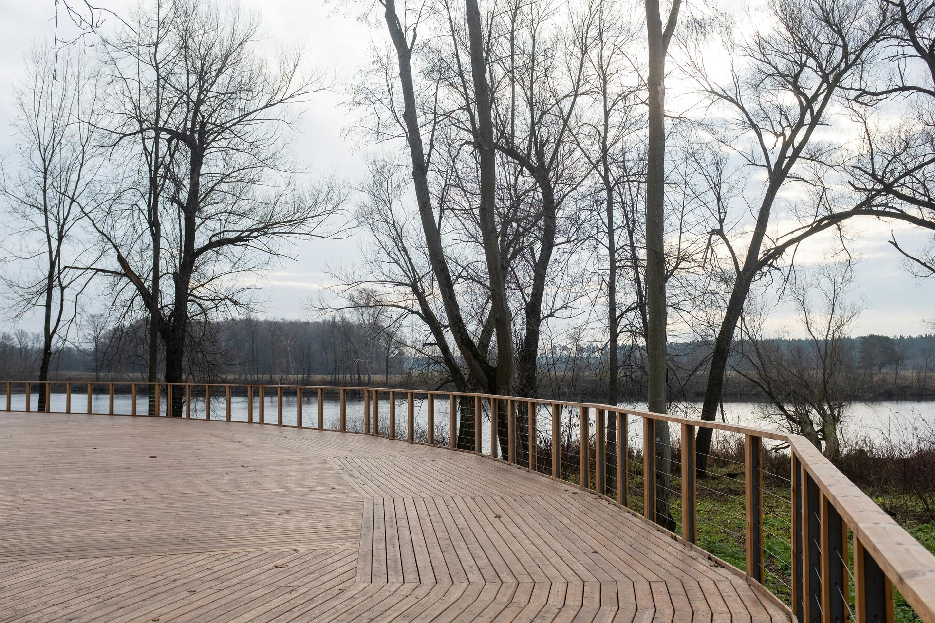 Curved wooden boardwalk overlooking a lake with bare trees and a cloudy sky
