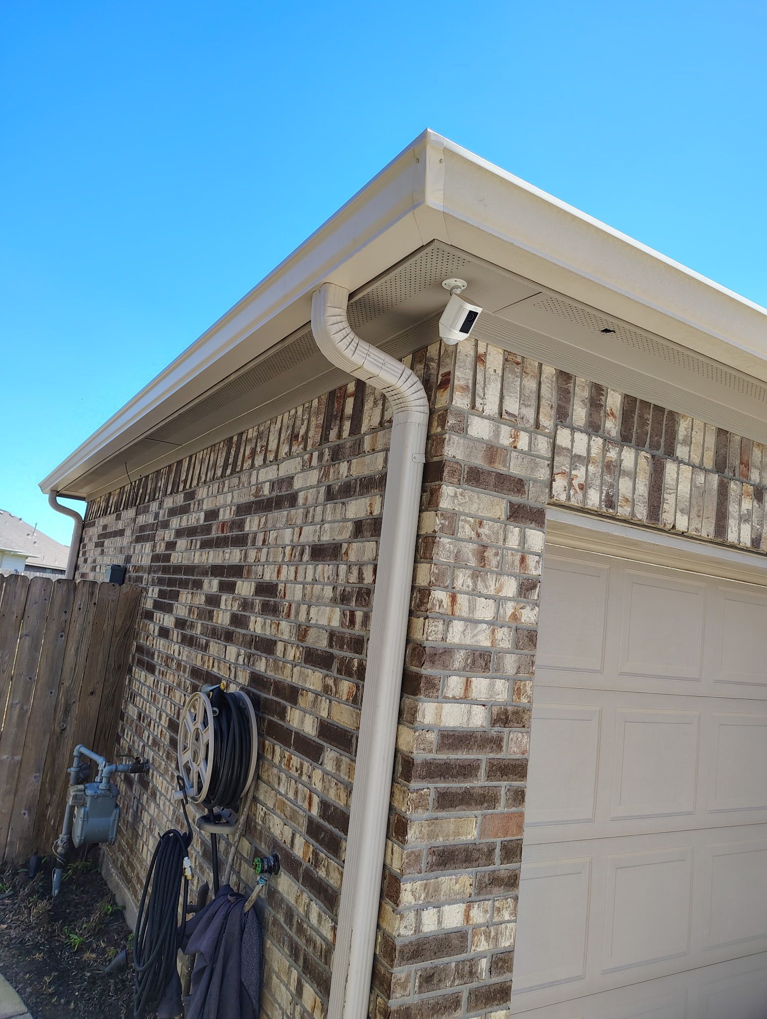 Brick building corner with white gutters, beige trim, and a clear blue sky.