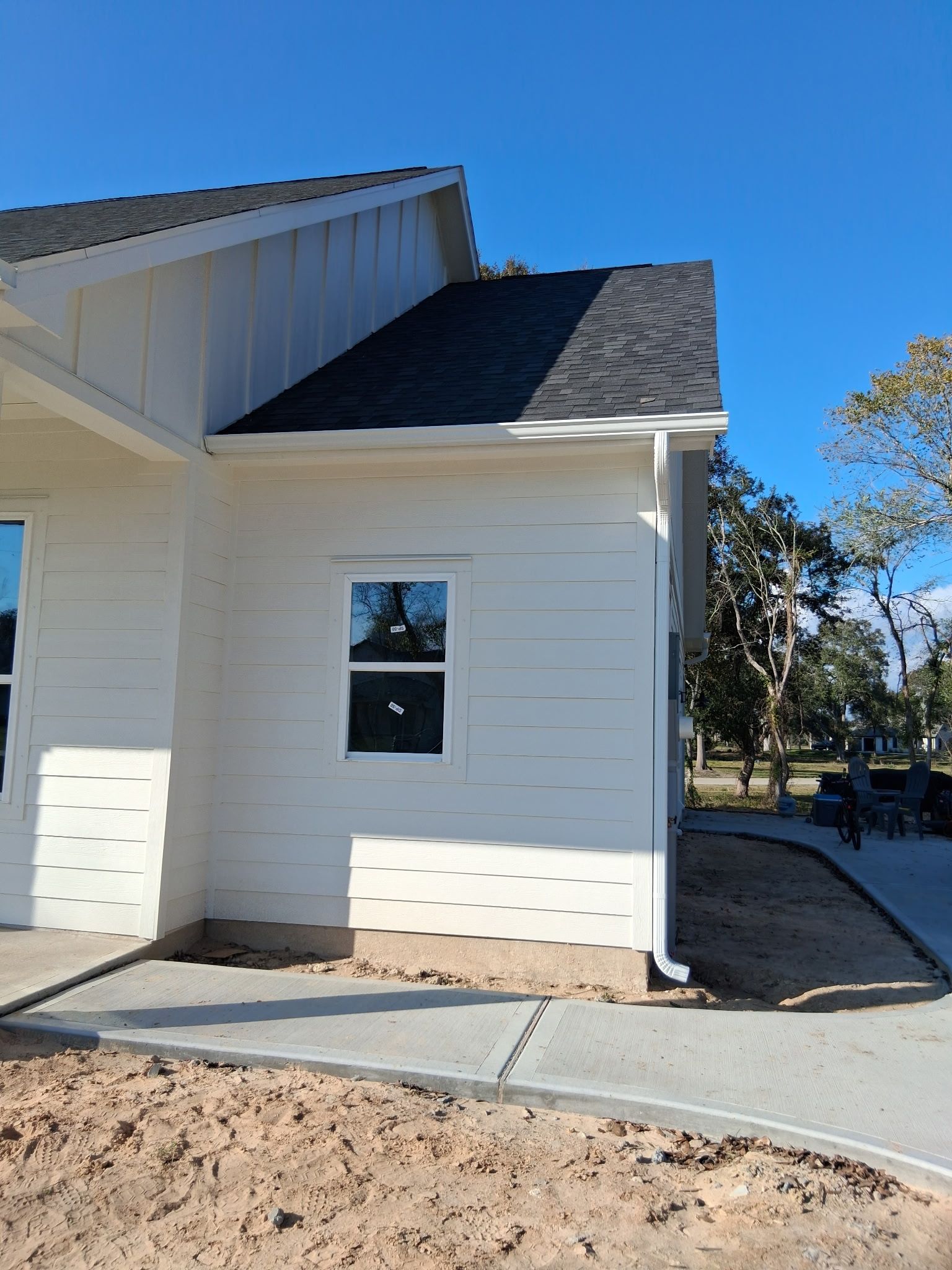 White house exterior with dark roof, a window, and concrete walkway under a blue sky.