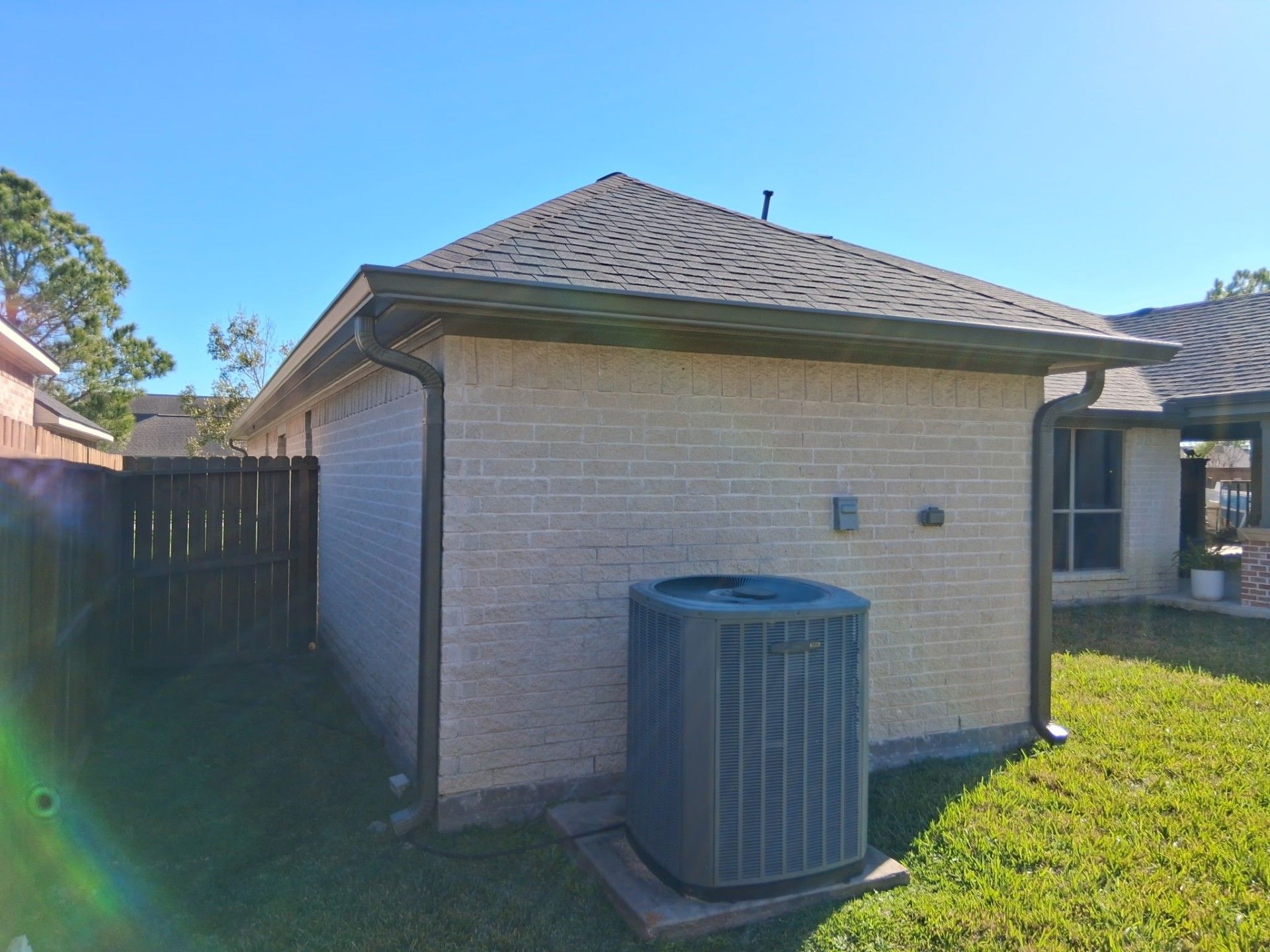 Brick building with brown roof, gutters, and AC unit on green lawn; sunny day.