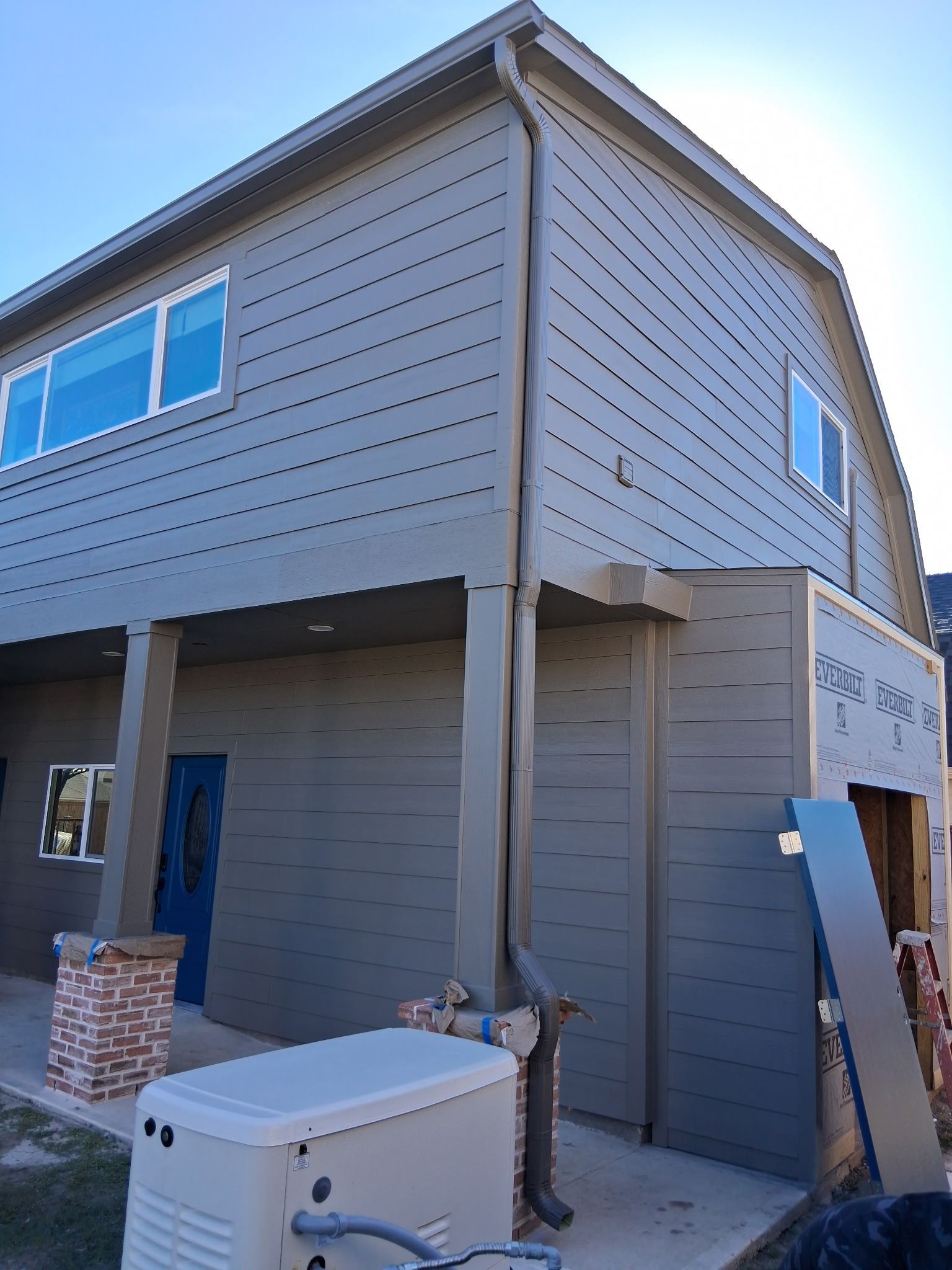 Exterior of a two-story building with gray siding, blue door, and brown trim.