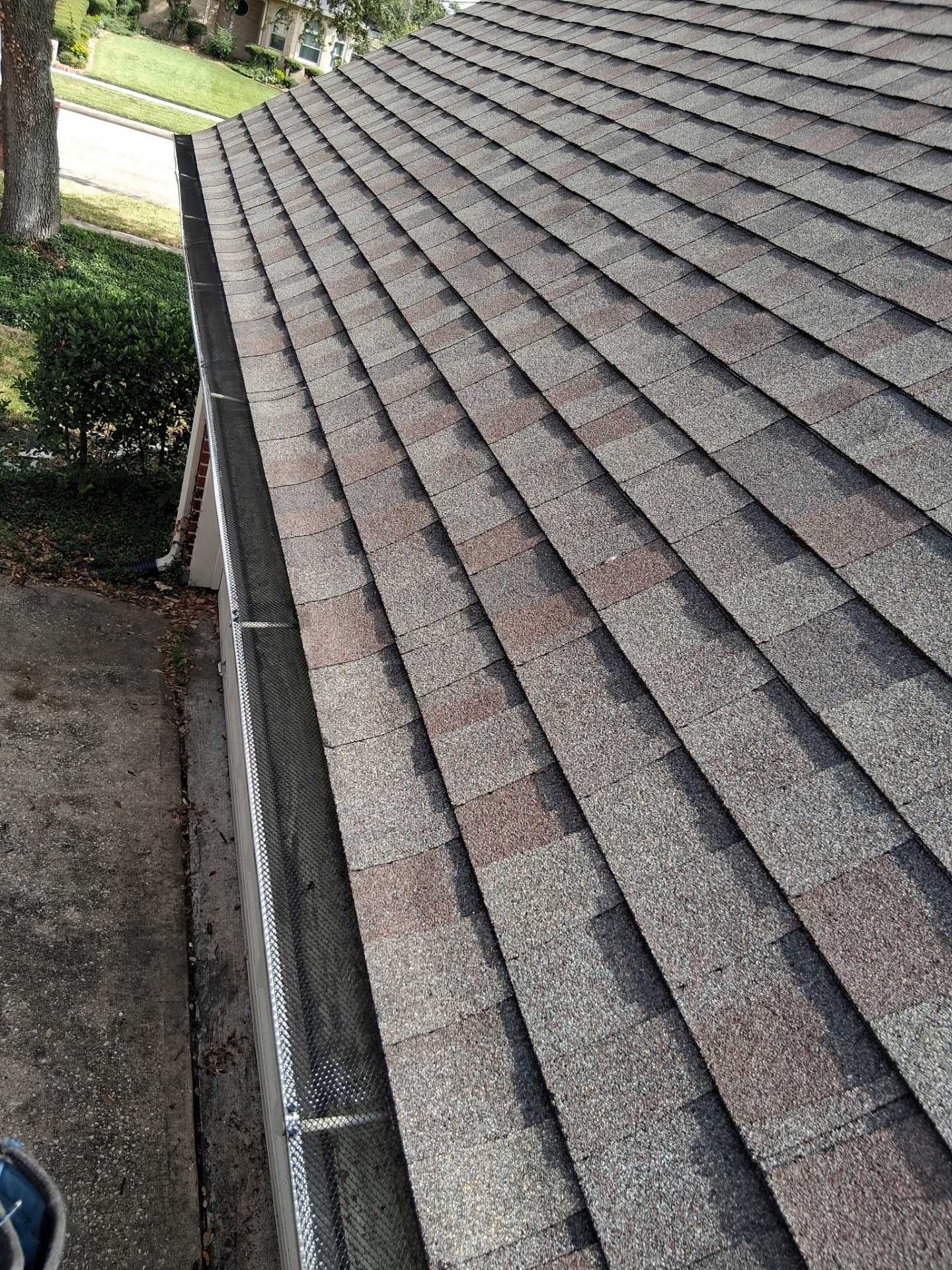 Close-up of a roof with brown and gray shingles. A gutter runs along the edge.