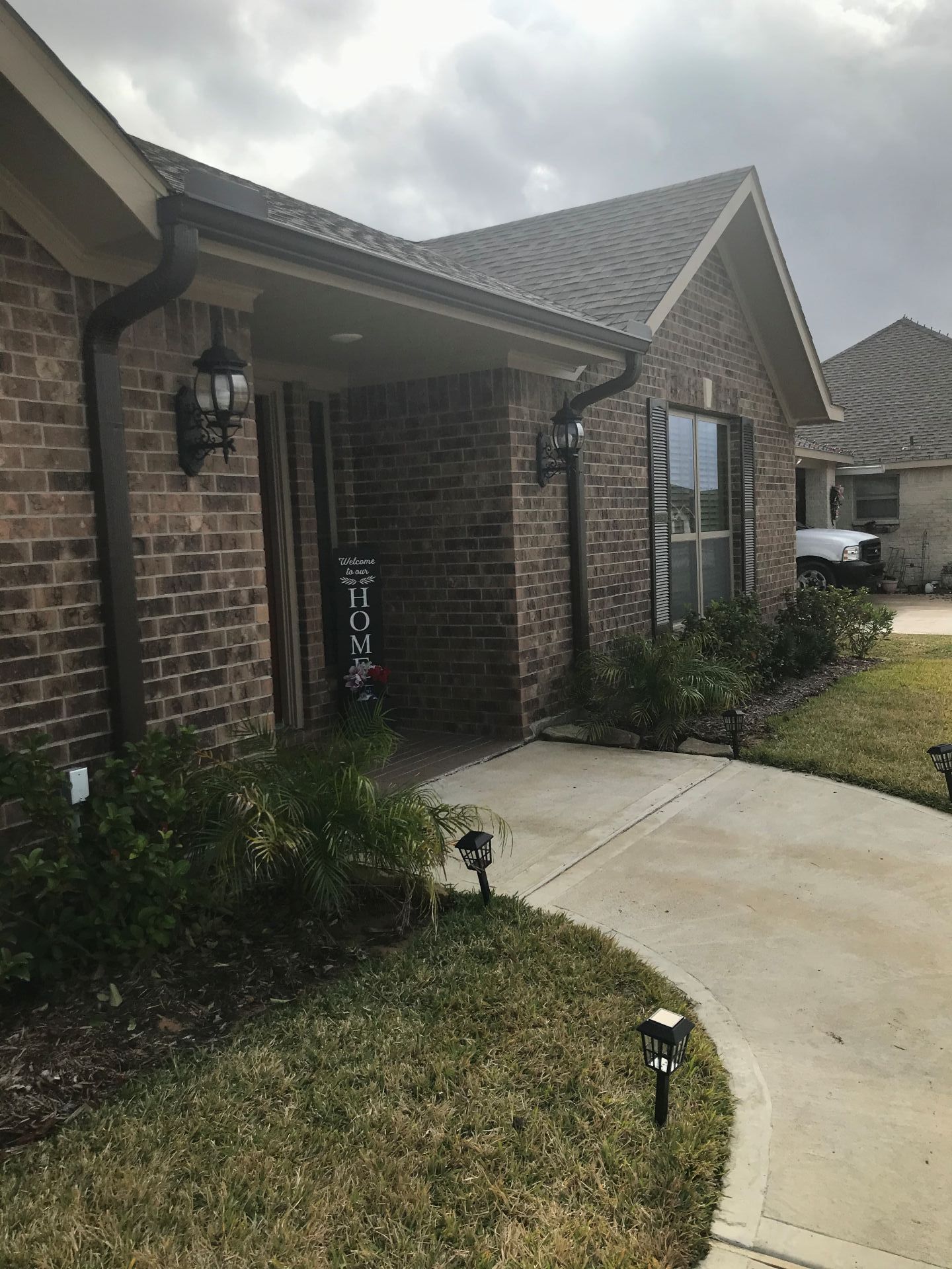 Brick house exterior with porch, dark gutters, and walkway leading to the entrance. 