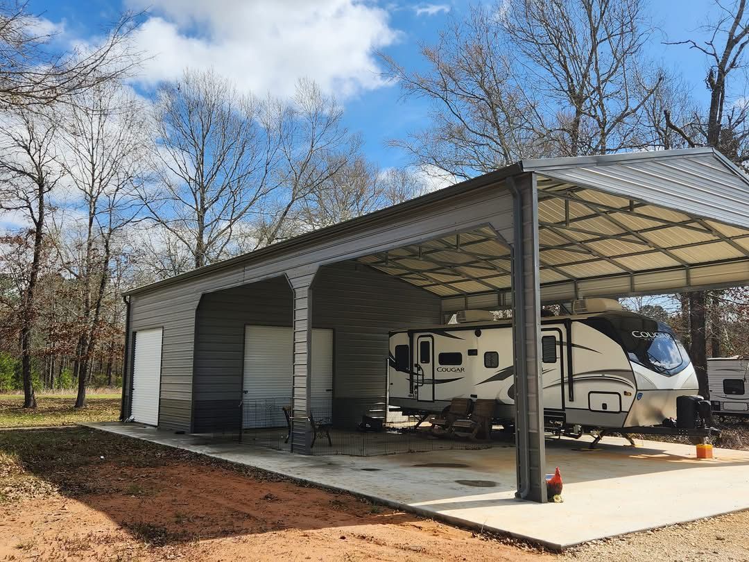 RV under a metal carport, trees in background, sunny day.